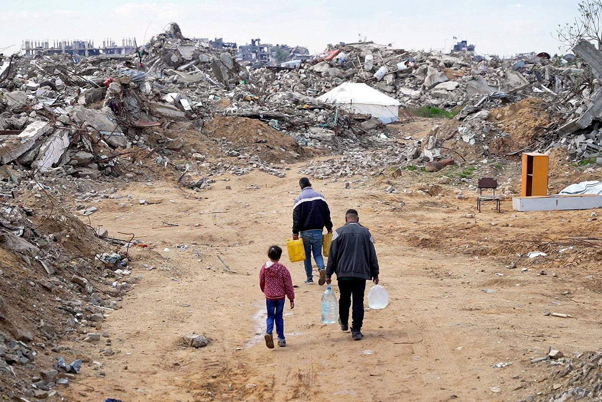 Family in Gaza carrying water containers through rubble